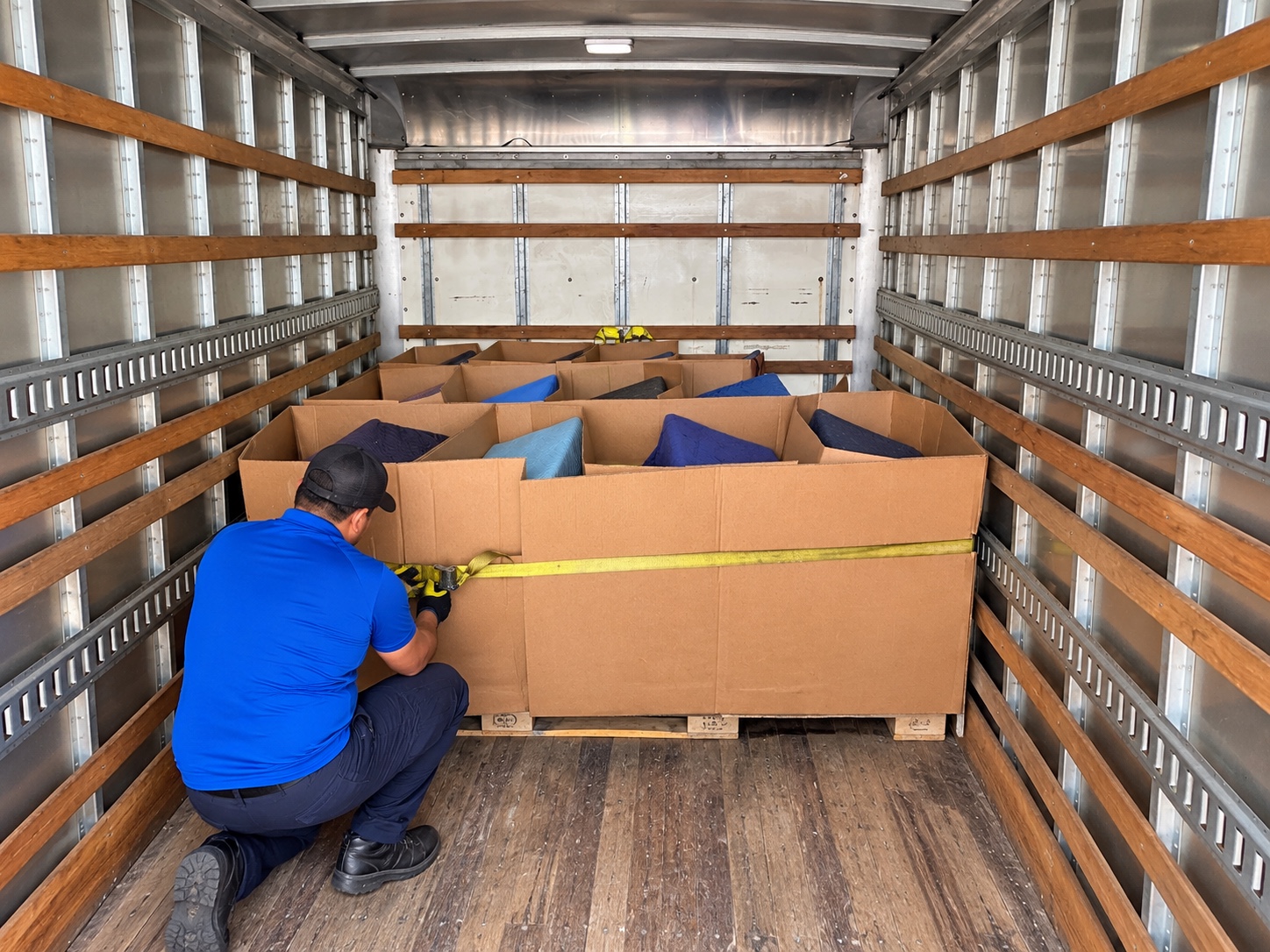 Worker securing protected furniture with a yellow strap inside the truck