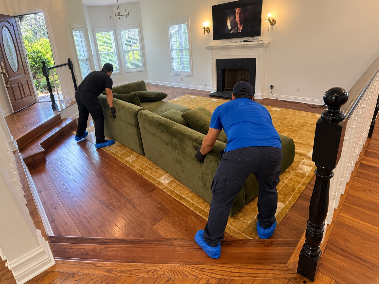 Two workers positioning a green sofa in a living room